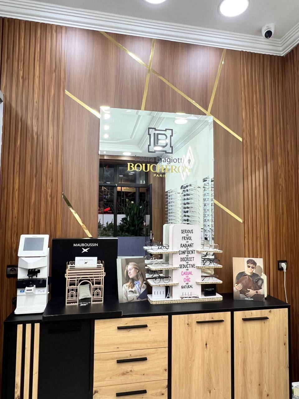 Le mur en noyer rainuré aux filets d'or de la boutique, miroir Boucheron et présentoirs de montures